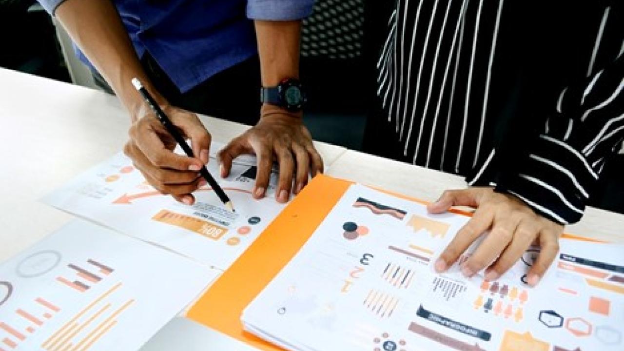 two people writing notes on papers with graphs and charts