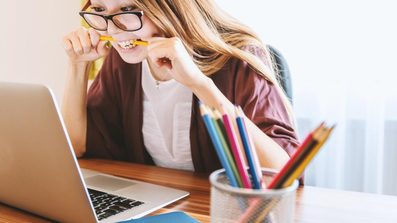 Woman at a laptop biting a pencil in frustration